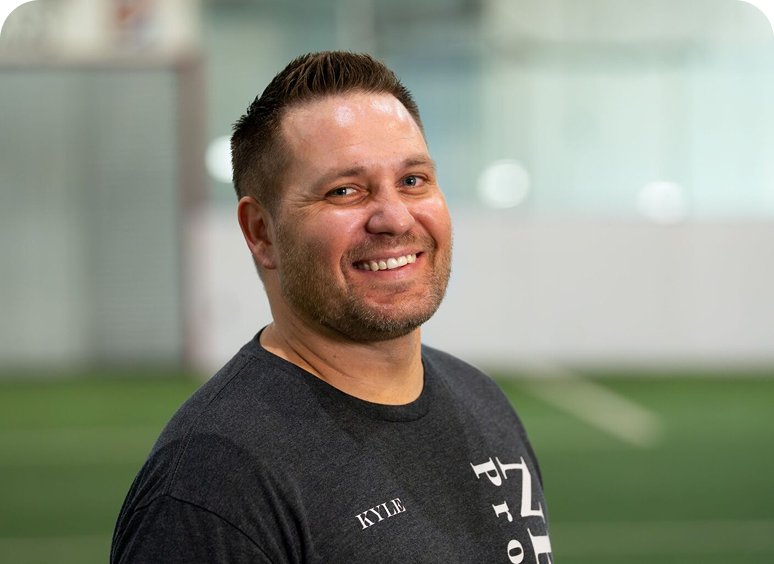 Smiling man indoors wearing a dark shirt.