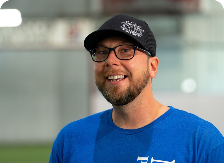 Man smiling, wearing glasses and a hat.