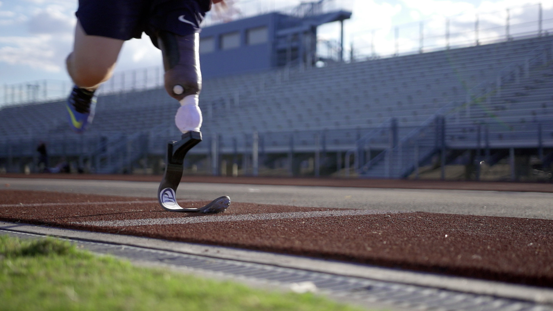 Athlete with prosthetic leg running on track.